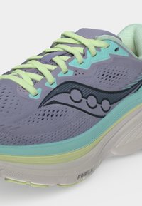 Gros plan d'une chaussure de course grise et turquoise avec des lacets jaunes, une tige en mesh et une semelle épaisse et rembourrée portant la mention PWRRUN.