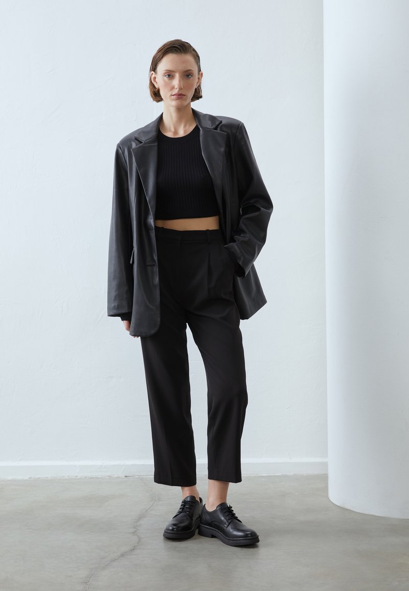 Black leather oversized blazer with structured shoulders, paired with fitted black trousers and black lace-up shoes. Textured ribbed crop top.