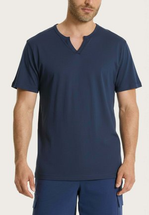 Uomo che indossa una maglietta blu scuro a maniche corte con scollo a V intagliato e pantaloni blu scuro abbinati con tasche laterali.