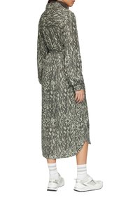 Pikk, lõtv rohelise värvi kleit mustade abstraktsete mustritega, millel on krae, pikad varrukad ja seotud vöökoht. Koos valgete tossudega.