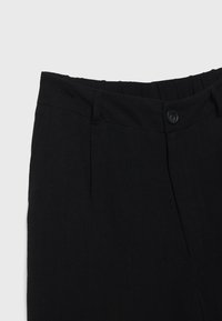 Pantalon noir avec fermeture à boutons et détail de taille élastique, présenté de la taille à mi-hanche sur un fond gris.