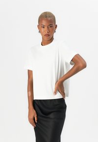 Weißes T-Shirt mit kurzen Ärmeln, aus Baumwolle, runder Ausschnitt, lockere Passform, kombiniert mit einem schwarzen Rock, glatte Textur, minimalistisches Design.