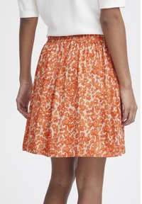 Květinová sukně s elastickým pasem, s jasně oranžovým a broskvovým vzorem. Lehce uvnitř s rozšířeným střihem.