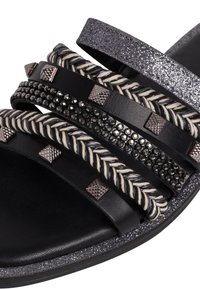 Svart halksandala med flera texturerade remmar med flätade detaljer, metallnabb och en glittrig sula för extra accent.