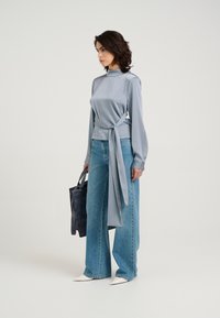 Lys grå satin langærmet top med bånd i taljen, parret med højtaljede blå vide jeans og hvide spidse sko. Sort tote taske.