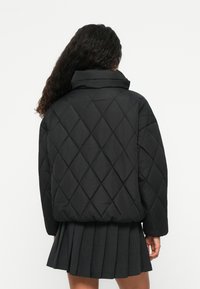 Μαύρο επενδυμένο πούφιν τζάκετ με ψηλό γιακά και χαλαρή εφαρμογή. Διαθέτει διαμαντένιο σχέδιο και ribbed μανσέτες, συνδυασμένο με μια πλισέ φούστα.