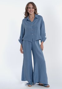 Camicia azzurro chiaro, aderente e morbida, con bottoni e maniche lunghe, dotata di una tasca, abbinata a pantaloni a gamba larga realizzati nello stesso tessuto.