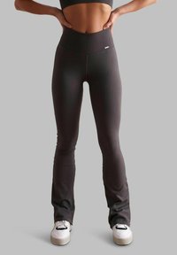 Leggings a vita alta in maglia grigia scura con una vestibilità aderente, apertura gamba svasata e branding sottile sulla vita, abbinati a sneakers bianche.
