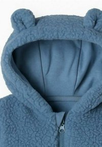 Capuche en polaire bleue avec des accents d'oreilles d'ours, comportant une doublure intérieure lisse et une fermeture éclair sur toute la longueur.