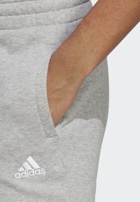 Pelēki sporta bikses, izgatavotas no kokvilnas maisījuma; ar sānu kabatām un baltu Adidas logotipu priekšpusē. Mīksta tekstūra un elastīgs jostasvieta.