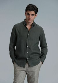 Donkergroene linnen shirt met een button-down kraag, voorzien van een slim fit en een gestructureerde stof. Gecombineerd met licht gestreepte broek.
