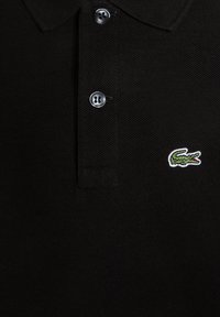 Black polo shirt made of textured fabric, featuring a three-button placket and a small green crocodile logo on the left chest.