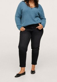 Maglione azzurro chiaro, con texture e scollatura a V, abbinato a jeans neri slim-fit. Le scarpe sono ballerine nere. Un outfit semplice e casual.