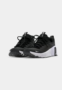 Zwarte sportschoenen van textiel met een gestructureerde stof, witte rubberen zolen, zwarte veters en contrasterende logo-details op de hiel.