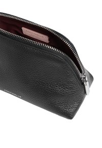 Pochette en cuir noir avec surface texturée, fermeture éclair argentée et doublure bordeaux. Présente un logo sur le devant et une petite étiquette intérieure.