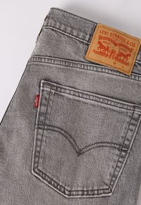 Γκρι τζιν Levi's δείχνει πίσω τσέπη, κόκκινη ετικέτα Levi's και καφέ δερμάτινο λογότυπο με το λογότυπο και λεπτομέρειες μεγέθους.