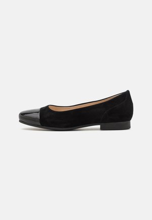Chaussure plate noire pour femme avec corps en daim et bout rond en cuir verni brillant, talon bas et design à enfiler.