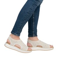 Sandales en tricot beige à conception ouverte, avec un dessus texturé et une semelle en caoutchouc blanche. Caractéristiques : découpes et sangle de cheville rembourrée pour plus de confort.