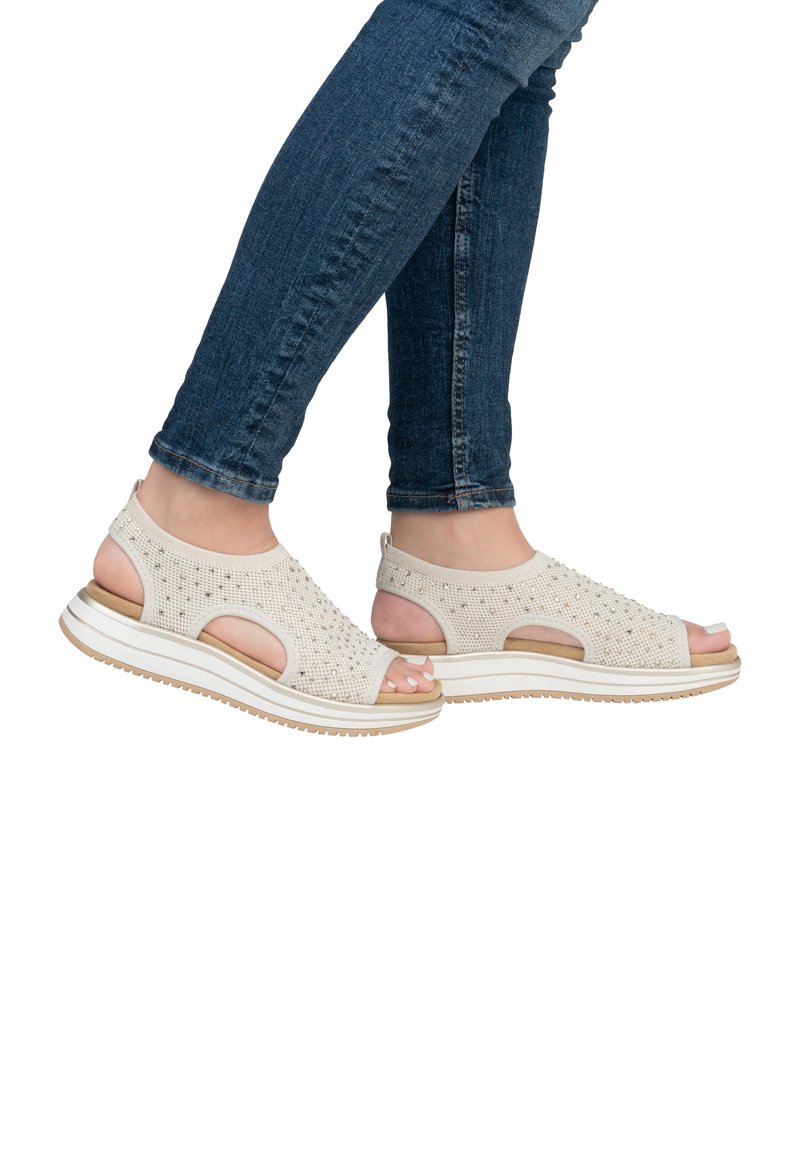 Sandales en tricot beige à conception ouverte, avec un dessus texturé et une semelle en caoutchouc blanche. Caractéristiques : découpes et sangle de cheville rembourrée pour plus de confort.