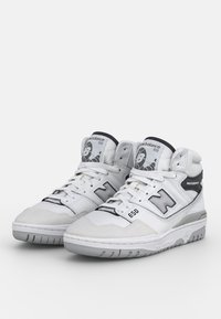 White high-top sneakers with leather and suede panels, gray accents, reinforced toe cap, and prominent “N” branding on the sides.