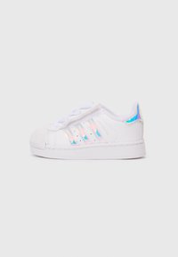 Baltie sneakers ar teksturētu gumijas purngalu, trim hologrāfiskiem svītrām un gludu sintētisku virsu. Ar sēju dizainu un mīkstinātu apkaklīti.