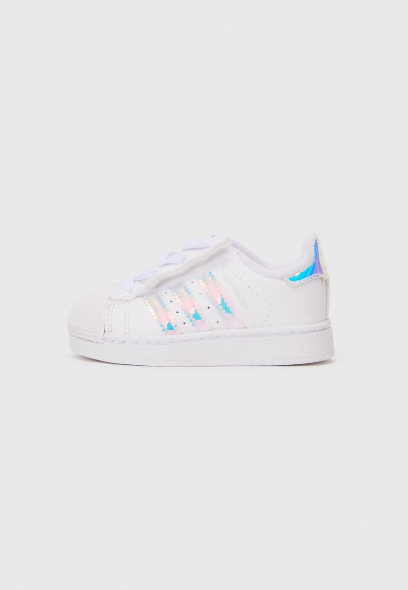 Baltie sneakers ar teksturētu gumijas purngalu, trim hologrāfiskiem svītrām un gludu sintētisku virsu. Ar sēju dizainu un mīkstinātu apkaklīti.