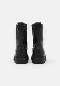 Mustat nahkasaappaat, jotka ulottuvat nilkkaan, paksuilla pohjilla, takavetoketjulla ja pienillä punaisilla, valkoisilla ja sinisillä logoilla takana.