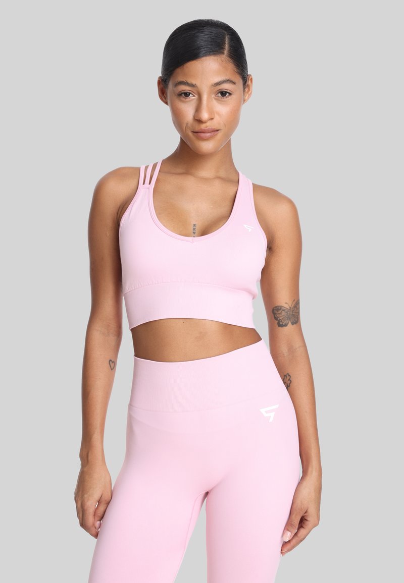 Jasnoróżowy stanik sportowy z okrągłym dekoltem i trzema cienkimi ramiączkami po każdej stronie, zestawiony z dopasowanymi legginsami z wysokim stanem z akcentami logo.