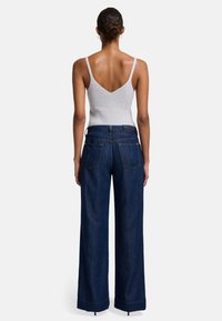 Dunkelblaue, weit geschnittene Jeans mit subtilem Muster, ergänzt durch ein enges, hellgraues Stricktanktop. Lange, gerade Silhouette mit genähtem Saum.