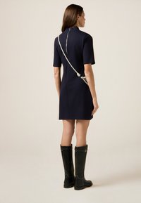 Granatowa sukienka z krótkim rękawem i wysokim kołnierzem, z dodatkowym srebrnym łańcuchem na plecach, w połączeniu z wysokimi, czarnymi botkami.