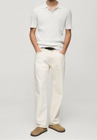 Polo à manches courtes blanc à côtes, pantalon droit couleur crème, et chaussures marron à enfiler, offrant un look propre et sobre.