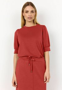 Top rosso a maniche corte con maniche a sbuffo, realizzato in tessuto morbido. Presenta un collo rotondo e una vestibilità rilassata, abbinato a una vita con cordoncino.