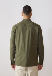 Camisa de manga larga verde oliva con una textura suave, puños abotonados y un cuello clásico, que presenta un dobladillo recto y un corte entallado.