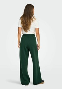 Grønne brede sweatpants med elastisk liv, lavet af blødt materiale, parret med en tætsiddende hvid kortærmet skjorte.