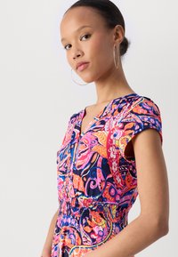 Robe multicolore à manches courtes, avec un motif abstrait vibrant en rose, bleu et orange. Taille élastique ; détail de boutons à l'avant.