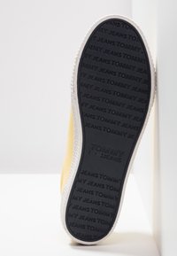 Yellow sneaker sole features a textured black rubber bottom with "TOMMY JEANS" embossed. The side shows a smooth fabric yellow upper and white outsole.