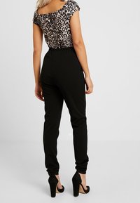 Černé tapered kalhoty s elastickým pasem, doplněné leopardím vrškem. Černé vysoké boty zvýrazňují outfit.