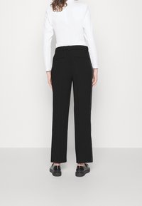 Zwarte brede broek met een ontspannen pasvorm, elastische tailleband en zijzakken. Draagt een witte top met lange mouwen. Gladde textuur.