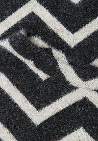 Pletená látka s černo-krémovým cikcak vzorem, chlupatou strukturou a měkkým vzhledem. Materiál vypadá silný a teplý.