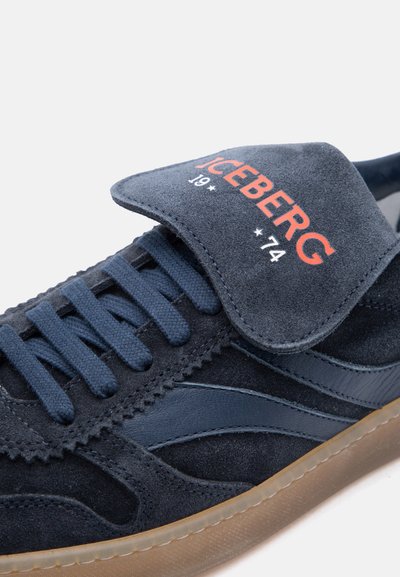 Baskets en daim bleu marine avec lacets assortis, semelle en gomme, et languette rabattable affichant "ICEBERG 19*74" en rouge et blanc.