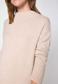 Maglione in cachemire beige chiaro con un collo alto a costine, vestibilità rilassata e polsini a costine. Texture morbida con un sottile motivo melange.