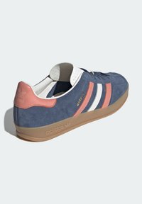 Námořnicky modrá semišová teniska s bílými a korálovými pruhy, vybavená polstrovaným límcem, gumovou podešví a zlatými logy. Klasický nízký střih.