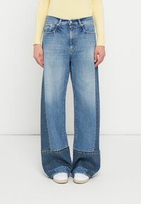 Φαρδιά τζιν παντελόνια σε ανοιχτό γαλάζιο χρώμα με εφέ ξεθωριάσματος, διαθέτουν υψηλή μέση, μπροστινές τσέπες και αντίθετες ραφές στο τελείωμα. Συνδυασμένα με λευκά παπούτσια.