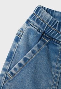 Denim püksid elastse vöökohtaga, helesinine värv, õrn pleekimine ja kontrastse kollase õmblusega. Omaduseks eesmine taskud ja vastupidav tekstuur.