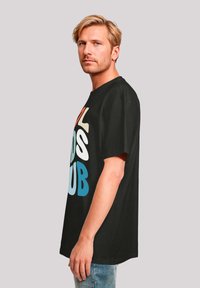 Black cotton t-shirt with bold, multi-colored text reading "ALL BIDS CLUB." Loose fit with short sleeves and a round neckline.