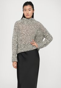 Grå og hvid strikket sweater med høj krave, løs pasform og ribbede manchetter, parret med en sort, strømmende nederdel.