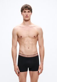 Μαύρα ανδρικά boxer briefs με καφέ ελαστική μέση που φέρει το λογότυπο "KARL LAGERFELD". Λείο ύφασμα, εφαρμοστή σχεδίαση, μήκος έως το μέσο του μηρού.