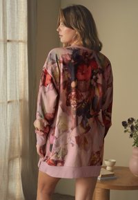 Oversized top s kvetinovým vzorom v odtieňoch ružovej a červenej, s balónovými rukávmi a mäkkou, texturovanou látkou. Spodný lem má jednofarebný ružový okraj.