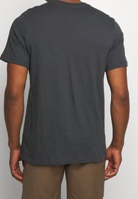 Mörkgrå bomullströja med korta ärmar, rundad halsringning och en mjuk textur, visad bakifrån.