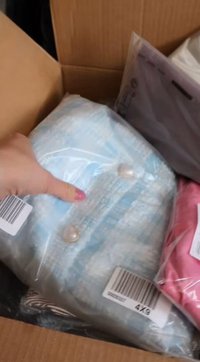 Šviesiai mėlyna drobė švarkas su perlų mygtukais, supakuotas į plastiką, šalia rožinės aprangos, kartoninėje dėžutėje.
